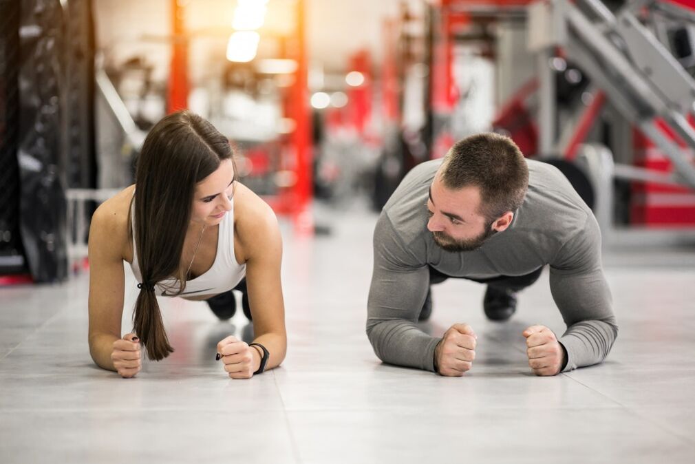 Чоловік і жінка виконують вправу «Планку», розраховану на всі групи м'язів. 